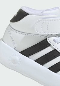 Białe trampki za kostkę z czarnymi paskami, rzepem i wytłoczonym logo po boku podeszwy.