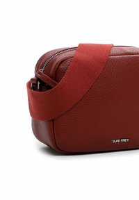 Borsa a tracolla rossa in pelle con superficie texturizzata, dotata di una spessa cinghia in tessuto e marchio in argento. Chiusura con zip nella parte superiore.