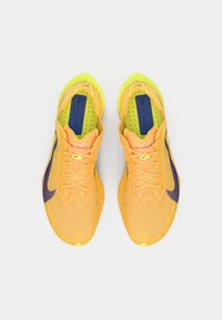 Svijetlo žute atletske tenisice s prozračnom mrežastom gornjištem, ljubičastim akcentima i teksturiranom potplatom. Sadrže vezice i podstavljeni ovratnik.