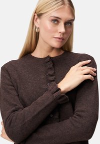 Cardigan marrone a maglia texturizzata con polsini a volant e chiusura con bottone. Scollo rotondo semplice e sottili variazioni di colore.