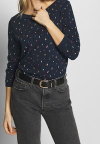 Marinblå mönstrad långärmad skjorta med färgglada prickar, ihop med högmidjade svarta denimjeans och ett svart bälte med en guldspänne.