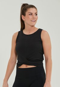 Svart ärmlös sporttank topp med rundad halsringning och en vriden framkant. Tillverkad av ribbat tyg med en mjuk yta.