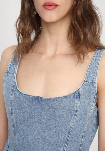 Denimkleit ruutjalga, laiade õlgadega rihmadega, helesinises värvitoonis, kerge tekstuuriga ja kontrastsete õmblustega.