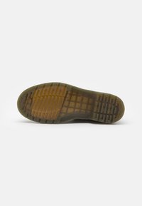 Semelle extérieure en caoutchouc brun avec un motif de grip texturé. Sections transparentes visibles, présentant des nervures et une empreinte de logo. Design robuste et matériau flexible.