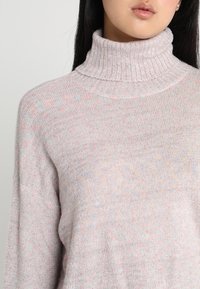 Hellrosa gestrickter Pullover mit hohem Kragen, lockerem Schnitt und dezenten mehrfarbigen Sprenkeln im gesamten Stoff.