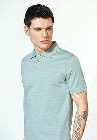 Jasnoniebieska koszulka polo z krótkimi rękawami, z dyskretnymi poziomymi paskami, klasycznym kołnierzykiem i zapięciem na trzy guziki.