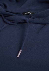 Felpa blu navy con una superficie liscia, cappuccio regolabile con inserti in metallo argento e un'etichetta vicino al collo. Design semplice e funzionale.