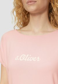 T-shirt rose à manches courtes en coton doux, arborant un logo blanc en écriture cursive "s.Oliver" sur le devant. Encolure arrondie, texture lisse.
