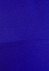 Tissu bleu roi vibrant avec une texture lisse, présentant un léger éclat. Une couture cousue traverse horizontalement la partie inférieure.