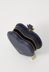 Herzförmiges, dunkelblaues Leder-Münzporto mit goldfarbener Reißverschluss und Beschlägen. Besitzt eine glatte Textur und ein geprägtes Logo auf der Vorderseite.