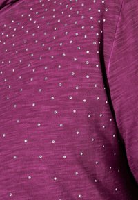 Violetti neulekangas, jonka pinnassa on rakenne, ja jossa on tasaisesti sijoitettuja hopeisia paljetteja.