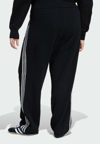 Čierne nohavice z waffle pleteniny s bielymi pruhmi po stranách a voľným strihom. Elastický pás a široké nohy, vhodné na neformálne nosenie.