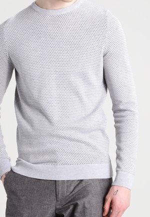 Hellgrauer Strickpullover mit strukturiertem Muster, Rundhalsausschnitt sowie gerippten Bündchen und Saum. Getragen über grauer Hose.
