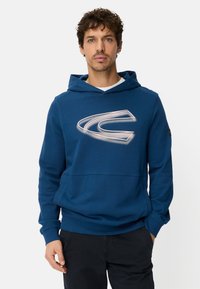 Blå sweatshirt med hætte og frontlomme, med en stor hvid logo på brystet. Fremstillet af blødt stof med en afslappet pasform.