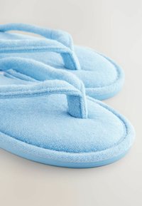 Chaussons en tissu bleu au texture douce, avec un design à lanières. Bords de semelle arrondis et garniture contrastante en bleu clair.