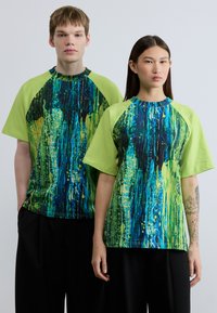 Γραφικά t-shirts με έντονο μπλε, πράσινο και κίτρινο αφηρημένο μοτίβο, με κοντά μανίκια και στρογγυλεμένο λαιμό.