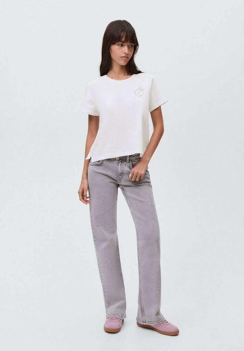 T-shirt en coton blanc avec un col rond et des manches courtes, associé à un jean gris clair et des chaussures roses. Design simple avec peu de détails.