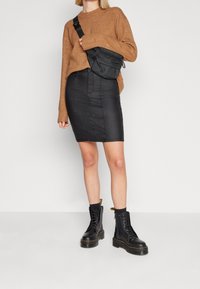 Brun stickad tröja, svart läderpennkjol och svarta snörstövlar med kraftig sula. Svart axelremsväska med dragkedja.