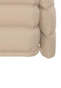 Beige puffer jacket sleeve and side with horizontal quilted stitching and a small circular logo near the hem.