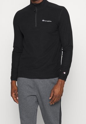 Černý dlouhý rukáv s čtvrtinovým zipem vyrobený z měkkého materiálu s logem Champion na levé části hrudníku a detaily loga na rukávu.