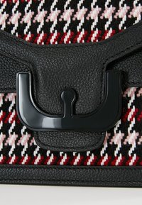 Gros plan de cuir noir et d’une boucle métallique sur un tissu texturé avec un motif pied-de-poule rouge, noir, blanc et rose.