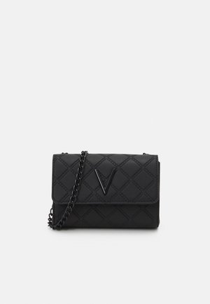 Small black quilted crossbody bag with flap closure, black chain strap, and black V-shaped logo on front center.