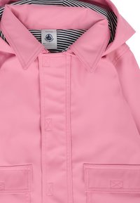 Giacca impermeabile rosa con fodera interna a righe, chiusura frontale con bottoni, due tasche a toppa e colletto strutturato. Texture liscia e lucida.