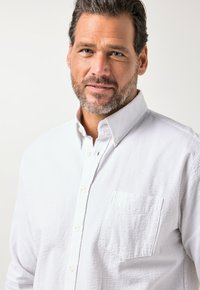 Weißes strukturiertes Hemd zum Knöpfen mit Brusttasche, klassischem Kragen und kleinen Knöpfen, gestaltet mit einem dezenten Prägungsmuster.