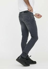 Graue Slim-Fit-Jeans mit glatter Textur, Fünf-Taschen-Design und dezenten Nähdetails, kombiniert mit schwarzen Sneakern.