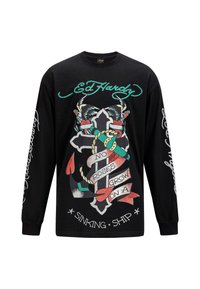 Schwarzes Langarmshirt mit auffälligen Grafiken eines Kreuzes, Schmetterlingen und Bändern mit Text. Bedruckte Akzente in Rot, Grün und Weiß.