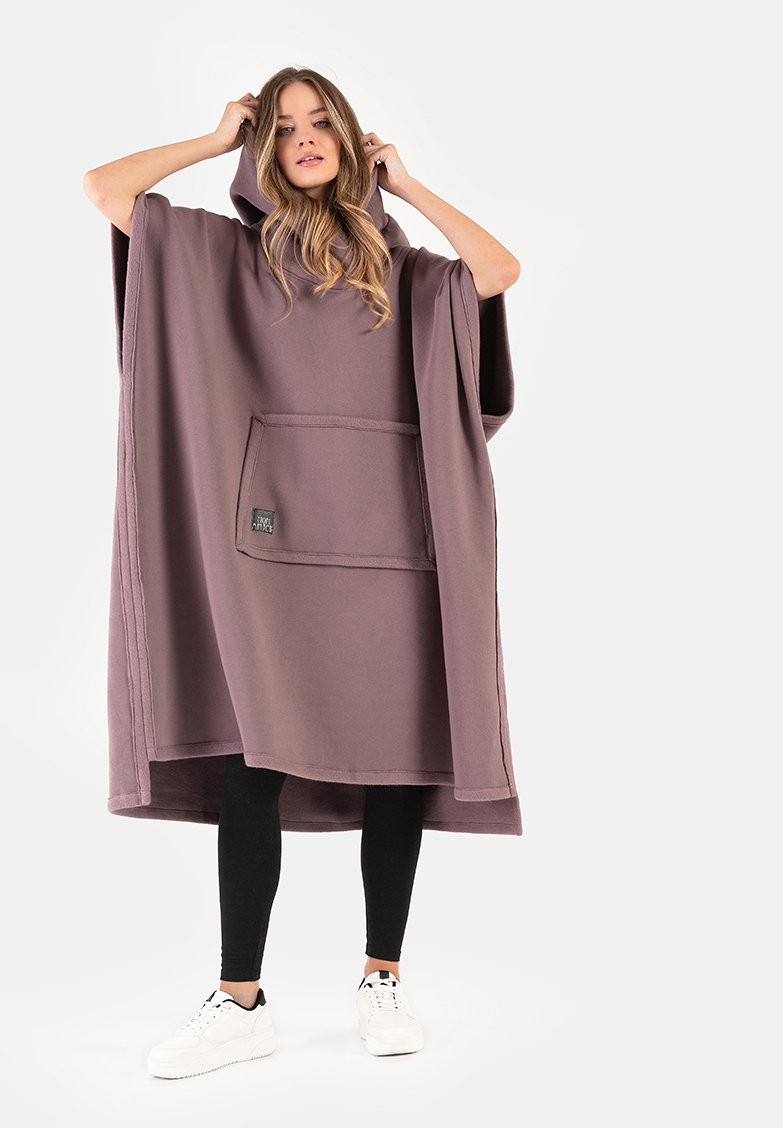 Nadmierny ponczo z kapturem w miękkim, stonowanym lawendowym materiale. Posiada przednią kieszeń, szerokie rękawy i luźny krój. Noszony na czarnych leginsach.