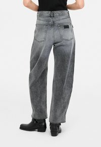 Augstās vidukļa, platās kāju džinsus izgatavoti no izbalējuša melnā denim ar vieglu mazgāšanas efektu. Iekļauj divas muguras kabatas un nelielu zīmola uzlīmi. Melni potīšu zābaki.