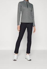 Black and white houndstooth-patterned long-sleeve top with a quarter zip, paired with slim black pants and white athletic shoes.