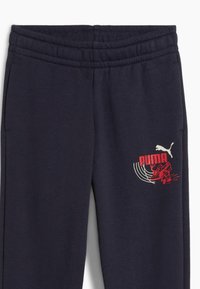 Granatowe spodnie dresowe z elastycznym paskiem w talii, z czerwono-białą grafiką logo Puma na lewym udzie. Miękki i wygodny materiał.