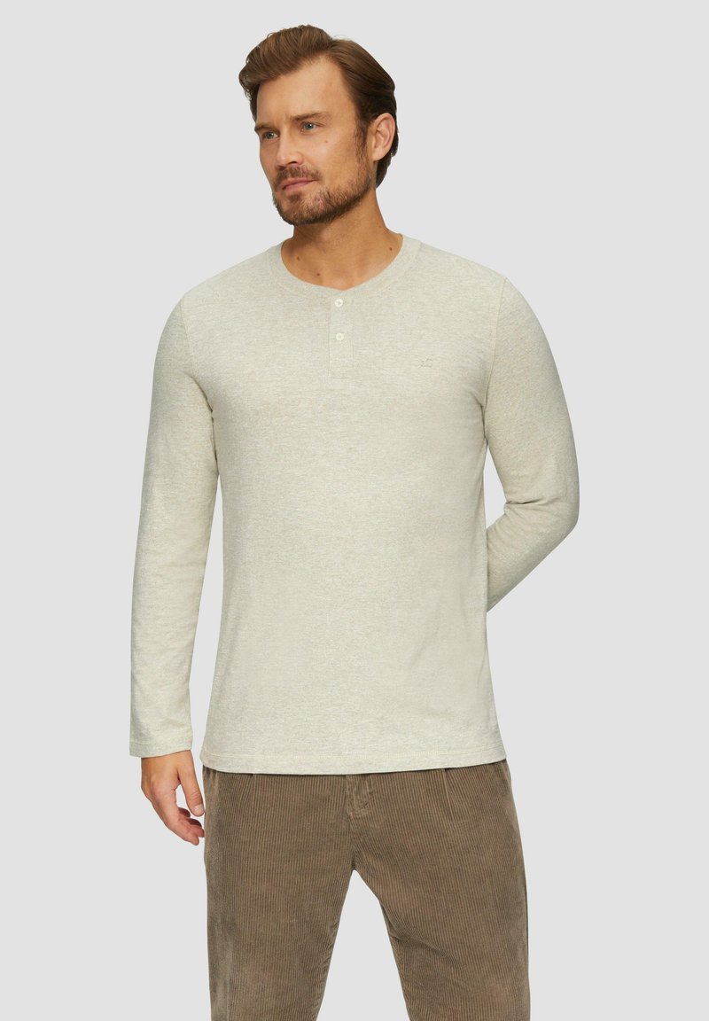 Langarm-Hemdd mit Rundhalsausschnitt in hellbeige, drei Knöpfen und weichem Textil, kombiniert mit braunen Cordhosen.