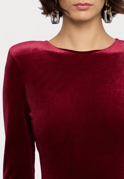 Burgunderfarbenes Samtkleid mit langen Ärmeln und einem Bootsausschnitt. Verfügt über metallische geometrische Ohrringe für zusätzliche Details. Weiche Textur.