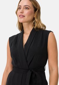 Svart ärmlös omslagsklänning med ett knytbälte, som har en djup V-ringning och en mjuk, flödande textur.