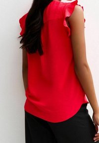 Rode top met korte mouwen heeft ruche schouders, textuurstof en een afgeronde zoom, gecombineerd met een aansluitende zwarte broek.