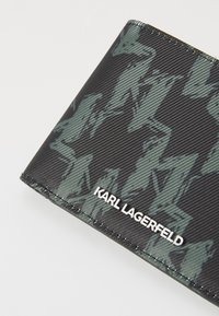 Portefeuille noir avec une finition texturée et un motif abstrait vert foncé. Le nom de la marque "KARL LAGERFELD" est imprimé en blanc.