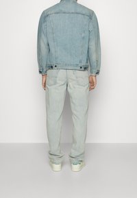 Ljusblå denimjacka med rak skärning och knappdetaljer, ihopparad med ljusblå jeans och beige sneakers med gröna accenter.