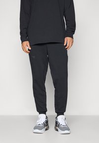 Black long-sleeve shirt paired with matching joggers featuring an embossed logo. Joggers have a tapered fit and side pockets. White sneakers complete the look.