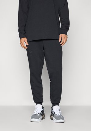 Black long-sleeve shirt paired with matching joggers featuring an embossed logo. Joggers have a tapered fit and side pockets. White sneakers complete the look.