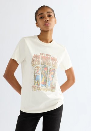 Vrouw draagt een wit T-shirt met kleurrijke vintage-stijl bogen en tekst "Let the Good Times Roll 19 Wrangler 47,", staand met handen in de heupen.