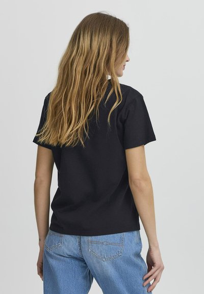 Tricou din bumbac negru, cu mâneci scurte, croială lejeră și tiv drept; asortat cu blugi albaștri deschis. Design simplu, fără logo-uri vizibile.