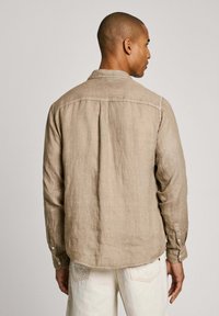 Camicia in lino khaki con spalla posteriore, polsini con bottone e vestibilità rilassata. Presenta una superficie leggermente testurizzata e dettagli di cucitura sottili.