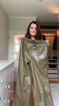 Kalhoty z umělé kůže v olivově zelené barvě s elastickým pasem, který má šňůrku a postranní švy, vystavené v jasné místnosti.