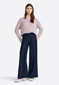 Lichtroze gebreide trui met een ontspannen pasvorm, gecombineerd met donkerblauwe wijde jeans met een gezoomde detail. Witte ballerina's maken de look compleet.