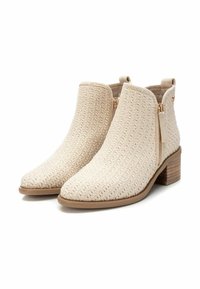 Botas de tobillo tejidas en color beige con puntera afilada, tacón de madera plano y cremalleras laterales. Parte superior texturizada y diseño minimalista.