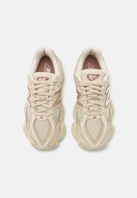 Beige sneakers feature a textured mesh upper with leather accents, round toe, and cushioned soles. Laces and branding in muted red.