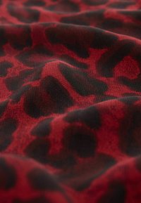 Roter und schwarzer Leopardenmuster-Stoff mit einer weichen Textur, der glatte, wellenförmige Bewegungen und deutlich definierte Musterkontraste aufweist.